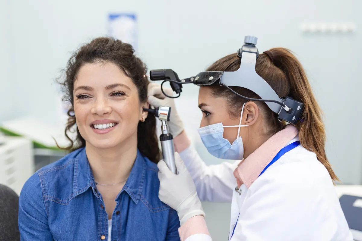 A hearing care professional looking into a smiling woman's ear with an otoscope