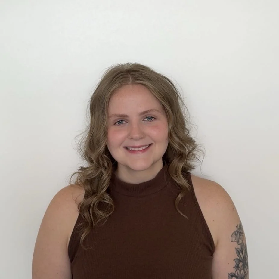 Mackenzie smiling in a brown sleeveless top against a plain white wall